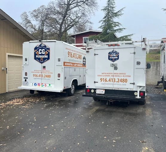 Two white CG Plumbing service trucks are parked side by side in a driveway. Both display the company logo, contact number, and service details in orange and blue text. Trees and houses are visible in the background.