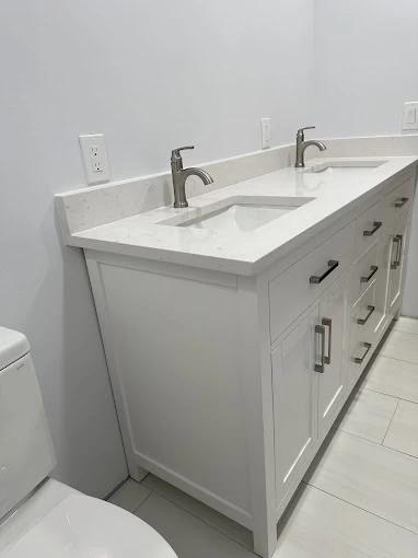White bathroom with a double-sink vanity, modern faucets, shaker-style cabinets, silver hardware, and a white countertop. For updates like this in CA, trust a plumbing contractor Sacramento County relies on for quality work.
