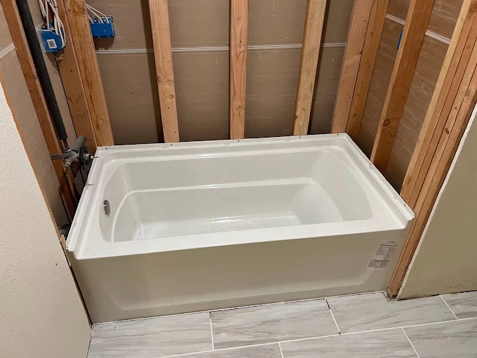 A white bathtub is installed in a CA bathroom under renovation, with exposed wooden wall studs and unfinished walls. The floor features light gray rectangular tiles—ideal for homeowners seeking plumber services El Dorado or Sacramento County.