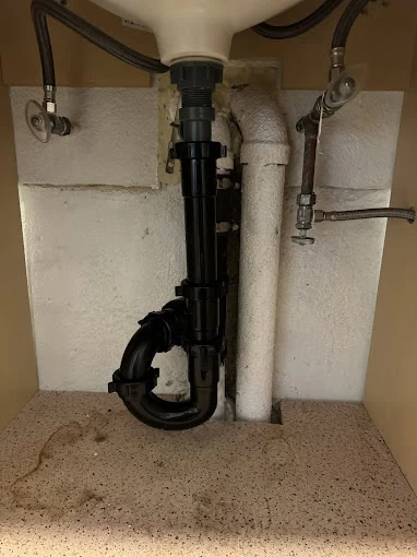 Under-sink view showing exposed plumbing, including black plastic pipes for drainage and metal supply lines. Installed against a white wall with a textured countertop, this setup reflects the quality of a trusted plumbing contractor Sacramento County.