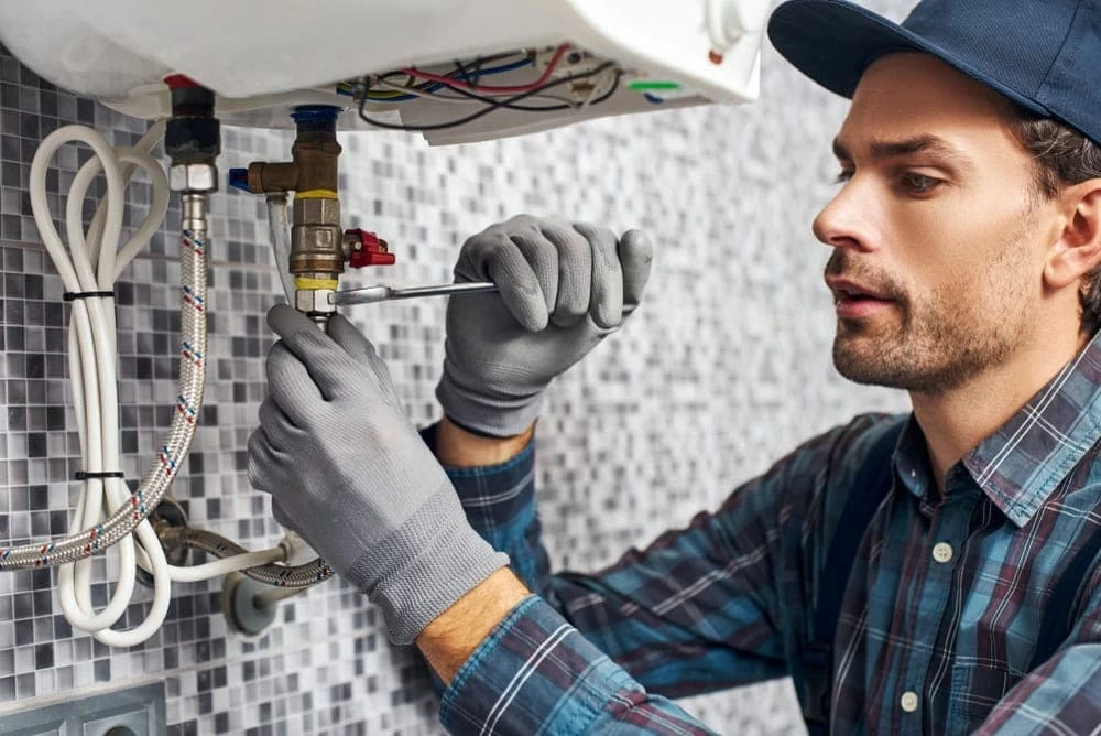 In this image, a professional plumber is shown inspecting and repairing a boiler system in a residential setting. He is using specialized tools—such as a wrench—to carefully adjust or tighten components, highlighting CG Plumbing’s thorough approach to boiler and heating system maintenance in El Dorado, CA.