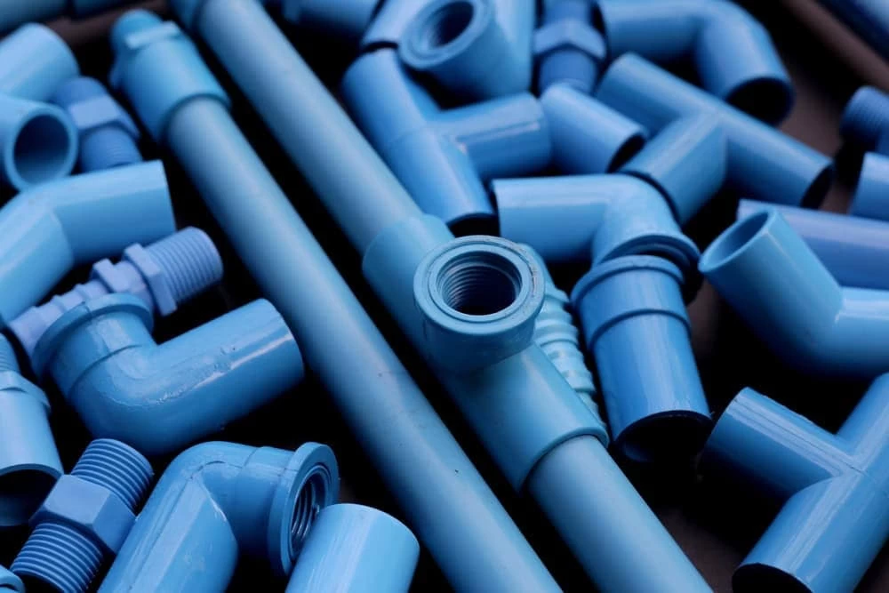 A collection of blue PVC pipes and pipe fittings, including elbows, tees, and connectors, arranged in a scattered manner.
