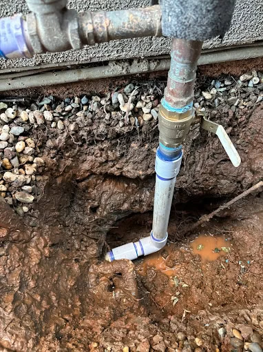 A water pipe with metal and PVC sections is shown outdoors, surrounded by wet, muddy soil and small rocks, indicating recent repair or a possible leak. A shut-off valve is attached to the pipe in El Dorado, CA.